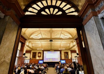 A view from the back of the room towards the screen in the UKFIET 2023 closing plenary. Picture also shows the arched window above the doorway and the ornate ceiling
