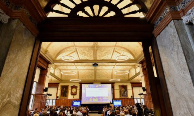 A view from the back of the room towards the screen in the UKFIET 2023 closing plenary. Picture also shows the arched window above the doorway and the ornate ceiling