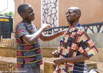 Young Ugandan man signs with his father. They are both wearing colourful shirts