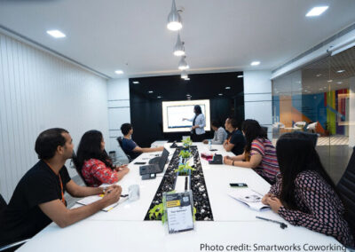 Colleagues sit and watch a presentation around a large table in an office, New Delhi, India