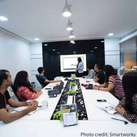 Colleagues sit and watch a presentation around a large table in an office, New Delhi, India