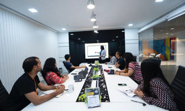 Colleagues sit and watch a presentation around a large table in an office, New Delhi, India