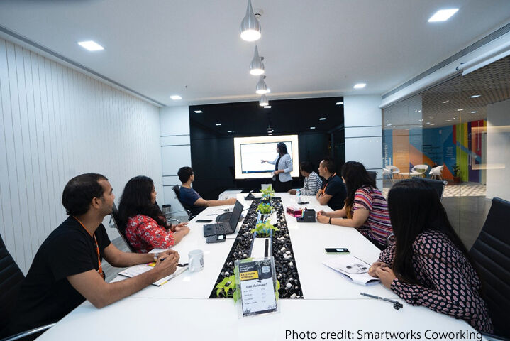 Colleagues sit and watch a presentation around a large table in an office, New Delhi, India