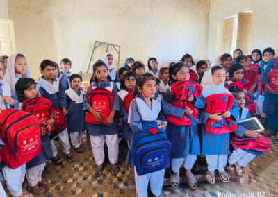 School children in blue uniforms hug their new red rucksacks in a classroom, Pakistan