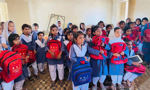 School children in blue uniforms hug their new red rucksacks in a classroom, Pakistan