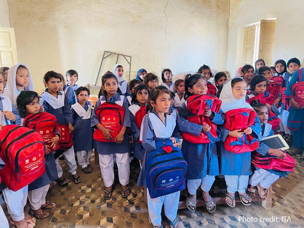 School children in blue uniforms hug their new red rucksacks in a classroom, Pakistan