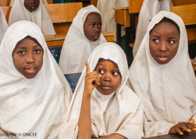 Children gather for Girls-for-Girls (G4G) peer mentoring sessions in Katsina state, Nigeria. School girls in white head scarves sitting at desk one with her finger up to ask a question