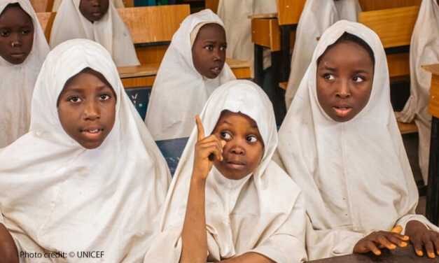 Children gather for Girls-for-Girls (G4G) peer mentoring sessions in Katsina state, Nigeria. School girls in white head scarves sitting at desk one with her finger up to ask a question