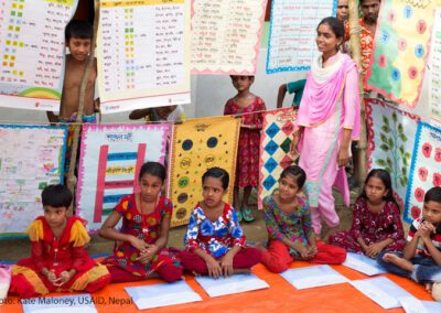 Children sit on the floor of a classroom in Nepal with posters hanging around them.