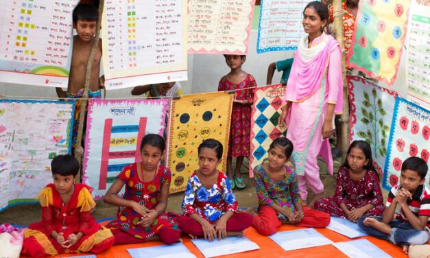 Children sit on the floor of a classroom in Nepal with posters hanging around them.