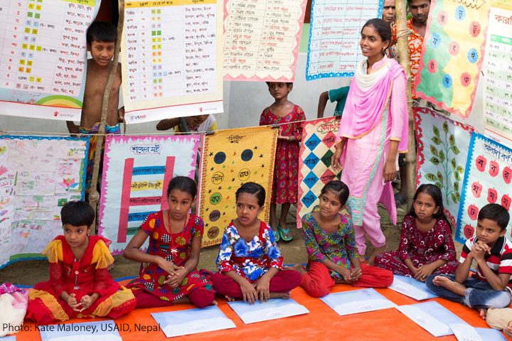 Children sit on the floor of a classroom in Nepal with posters hanging around them.