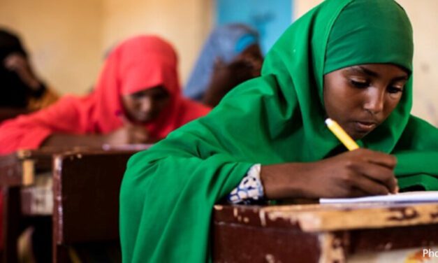 Alt text: Girls sit working at their desks in a classroom in Somalia. Girl in foreground wearing a green hijab