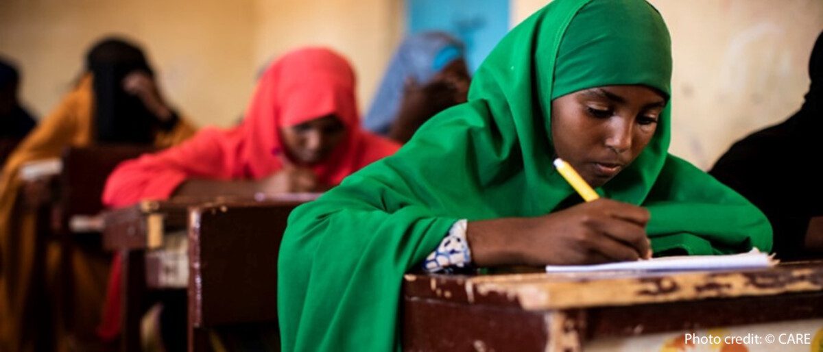 Alt text: Girls sit working at their desks in a classroom in Somalia. Girl in foreground wearing a green hijab