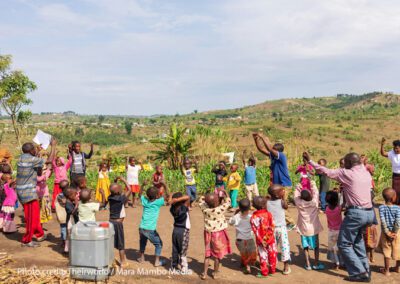 Colourfully dressed children play with their teachers in a circle, rural Uganda.