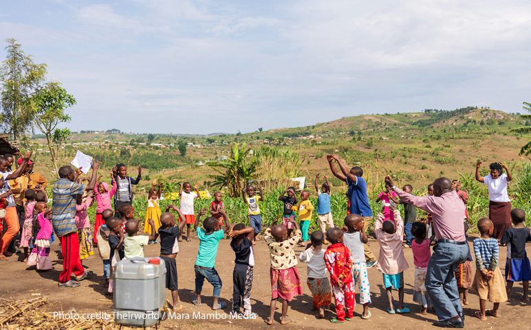 Colourfully dressed children play with their teachers in a circle, rural Uganda.