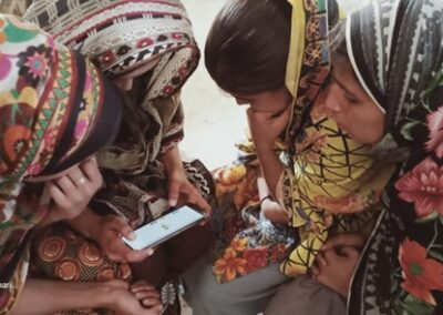 a group of girls gather around a mobile phone to engage with learning through the app, Pakistan.