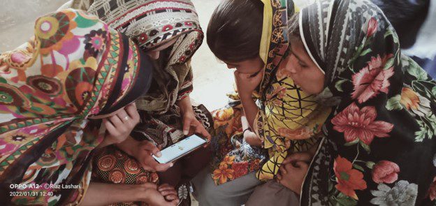 a group of girls gather around a mobile phone to engage with learning through the app, Pakistan.