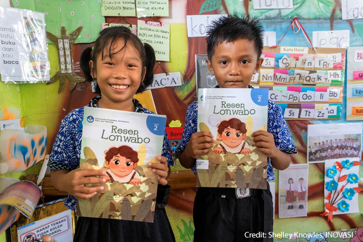 A young girl and boy hold up their textbooks in their classroom, Indonesia.