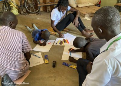 Children with disabilities engage in participatory research facilitated by peer researchers in Kenya. A group of adults and children working on the floor with coloured pens and paper