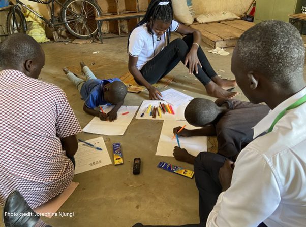 Children with disabilities engage in participatory research facilitated by peer researchers in Kenya. A group of adults and children working on the floor with coloured pens and paper