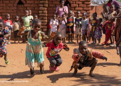 A few young children dance while others stand around them in a circle and watch, rural Malawi.