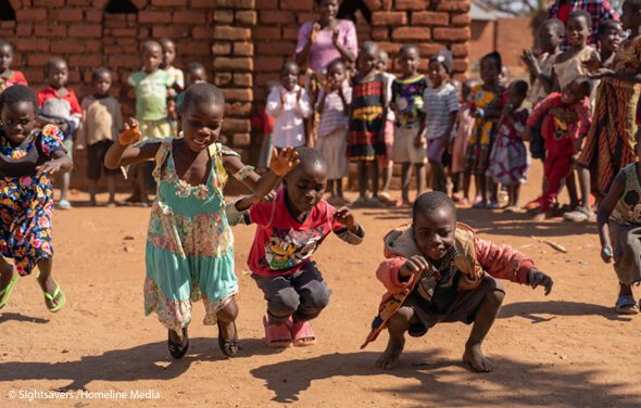 A few young children dance while others stand around them in a circle and watch, rural Malawi.