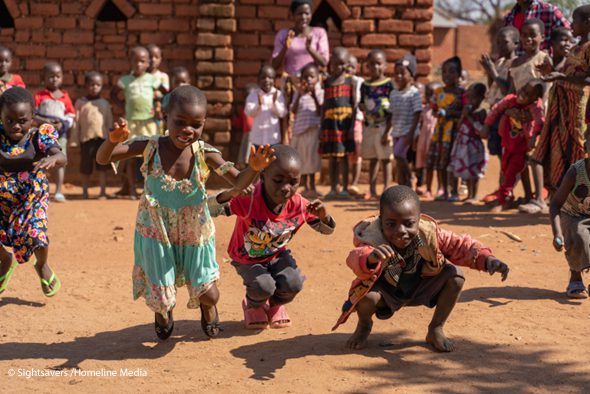 A few young children dance while others stand around them in a circle and watch, rural Malawi.