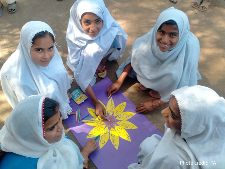 a group of girls sit around and create a flower with each petal being a key positive character attribute, such as: loving, bold, lovely good friend, strong, bold, etc.