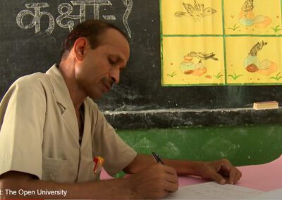 A male teacher writes in a classroom. Taken through the UK-Aid-funded TESS-India project, and a still from a video about TESS-India.