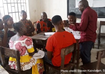 A group of teachers sit around a table in a classroom, engaging in a training workshop, Sierra Leone.