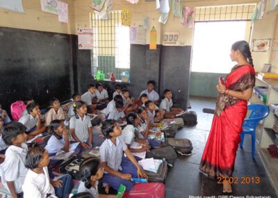 A female teacher stands at the front of the class with her students sitting on the floor in Chennai, India.