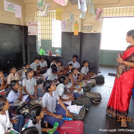 A female teacher stands at the front of the class with her students sitting on the floor in Chennai, India.