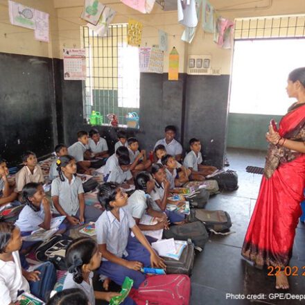 A female teacher stands at the front of the class with her students sitting on the floor in Chennai, India.