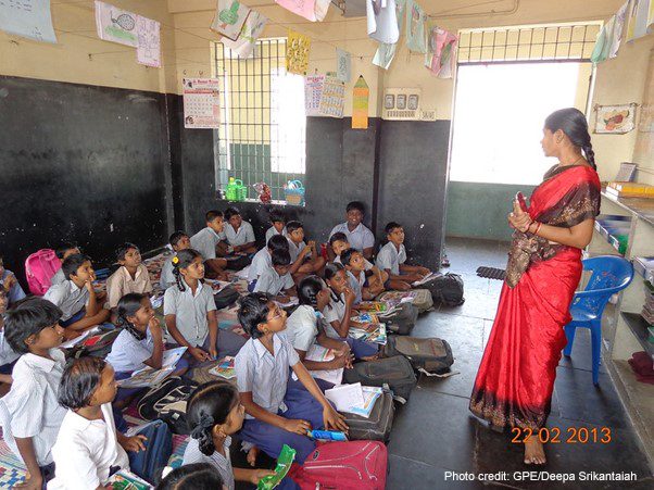 A female teacher stands at the front of the class with her students sitting on the floor in Chennai, India.