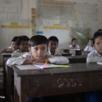 Young boys and girls sit looking out over their desks in class, Cambodia.