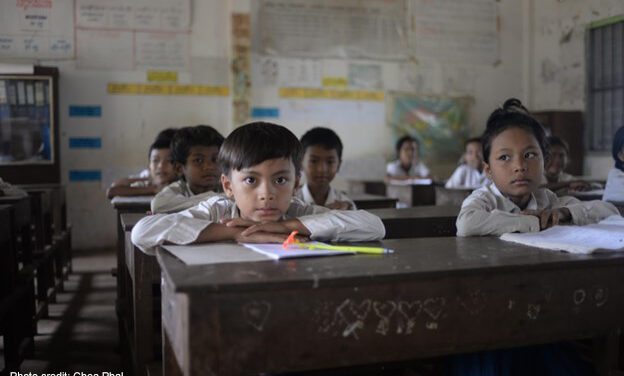 Young boys and girls sit looking out over their desks in class, Cambodia.