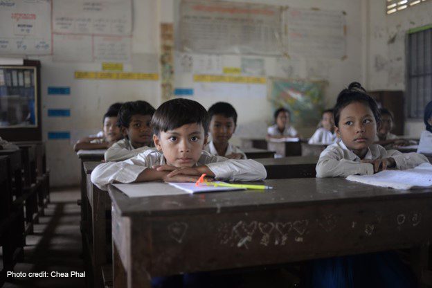 Young boys and girls sit looking out over their desks in class, Cambodia.