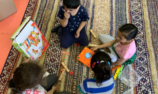 A group of young children sit together playing on a rug, Moldova.