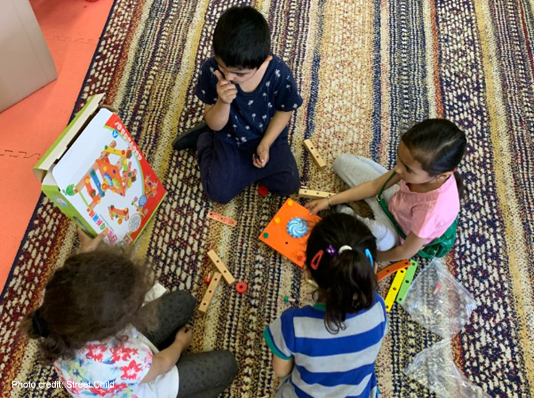 A group of young children sit together playing on a rug, Moldova.