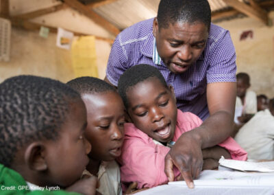 Students with teacher and textbook following her finger to read text at. Kasakola Primary School, Mpanda, Katavi, Tanzania.