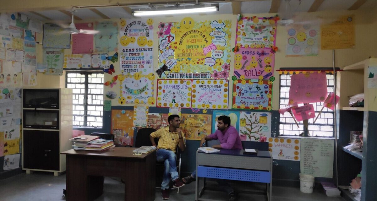 Two male teachers sit in a classroom and compare notes, India.