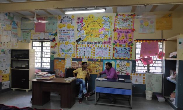 Two male teachers sit in a classroom and compare notes, India.