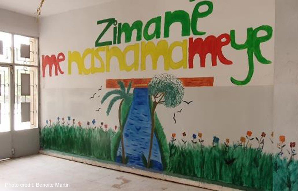 Mural on a wall in a Corridor in the school run by AANES in Qamishli. "Zimane me Nasnama me ye" with a meadow and a stream with trees.
