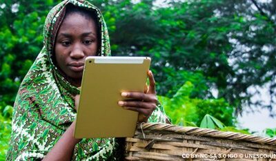 A young woman looks at course work on a tablet, while outside on her farm.