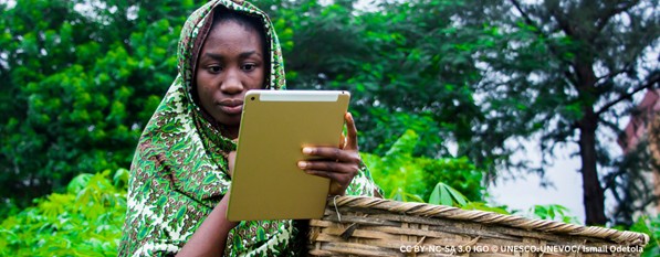 A young woman looks at course work on a tablet, while outside on her farm.