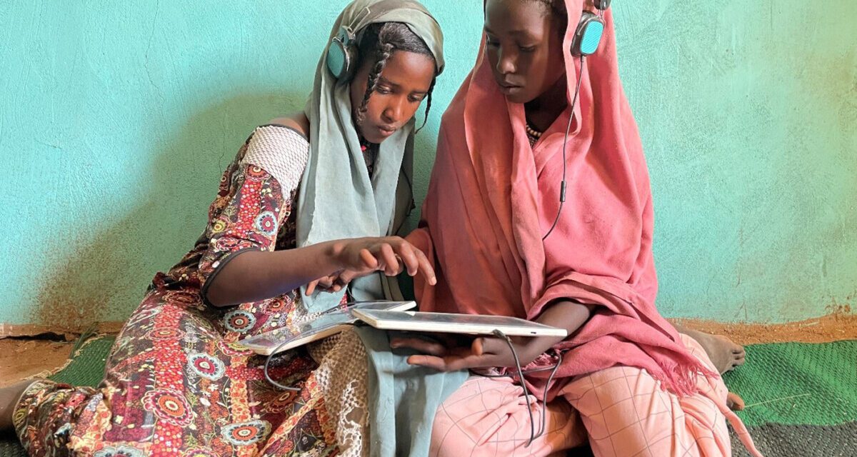 two girls with headsets and tablet devices sitting on the floor