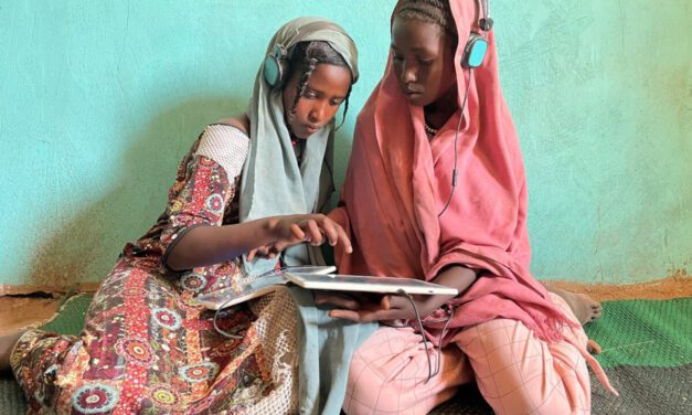 two girls with headsets and tablet devices sitting on the floor