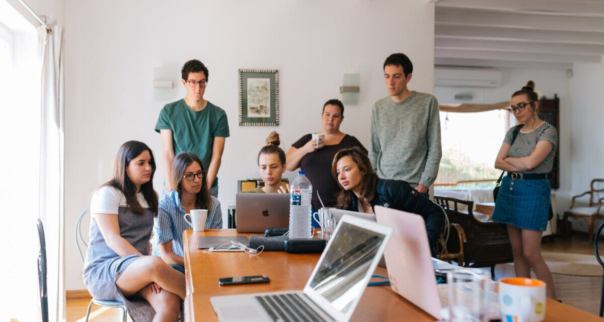 A group of students stand around laptops doing group work.