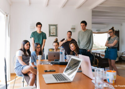 A group of students stand around laptops doing group work.