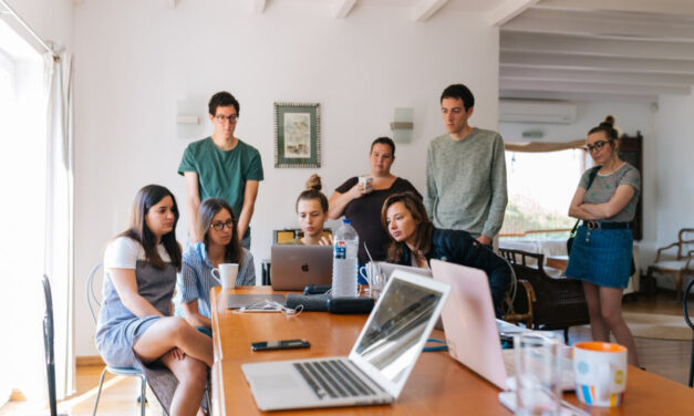 A group of students stand around laptops doing group work.